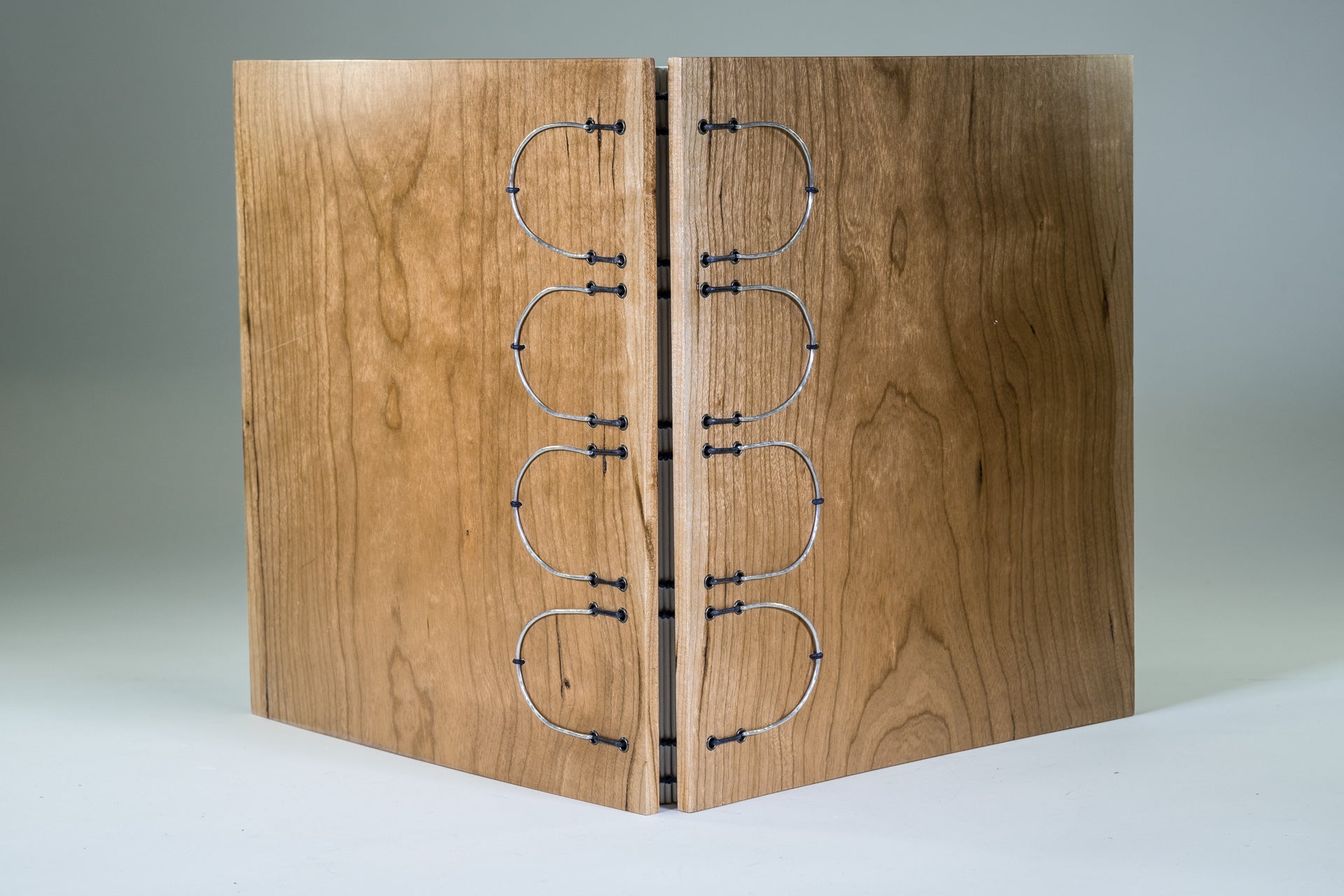 larger book with wood covers, bound on leather cords, hand-hammered metal hardware