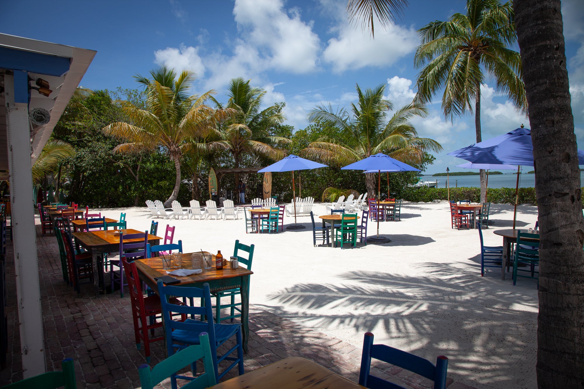 Florida Keys outdoor dining area with colorful tables and chairs under palm trees and blue umbrellas. Photographer Rick Graves