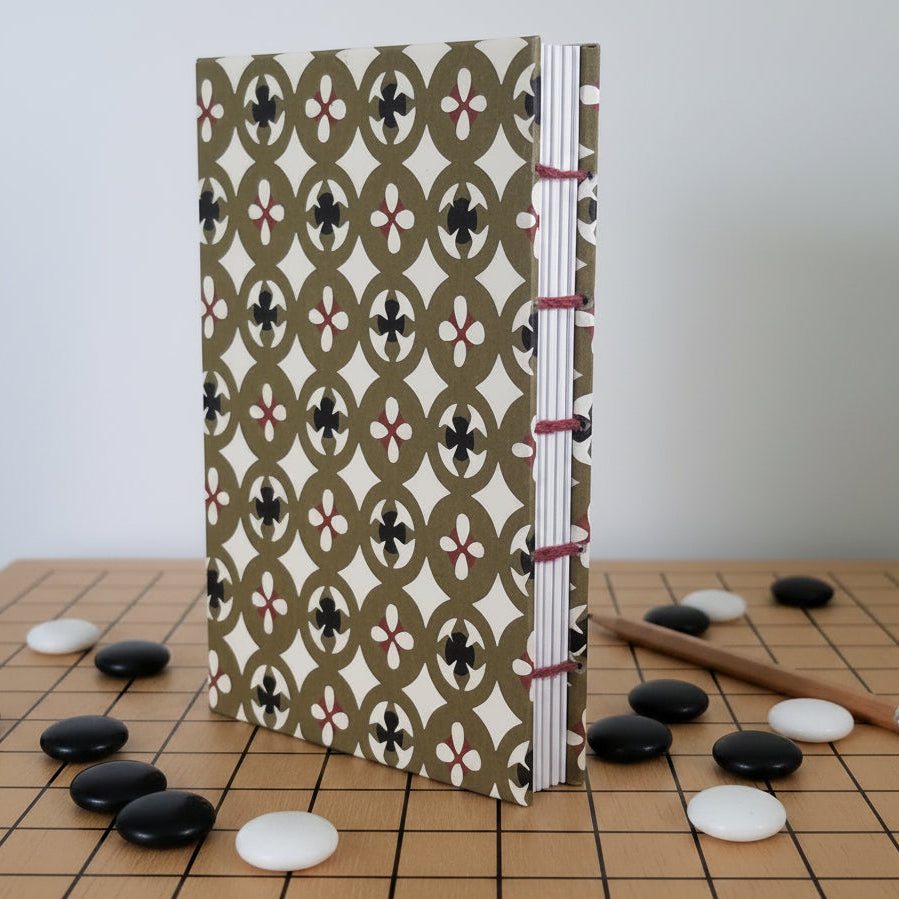 A similar book, computer-generated to stand on a Go board, with scattered pieces, and a pencil for keeping score of games.
