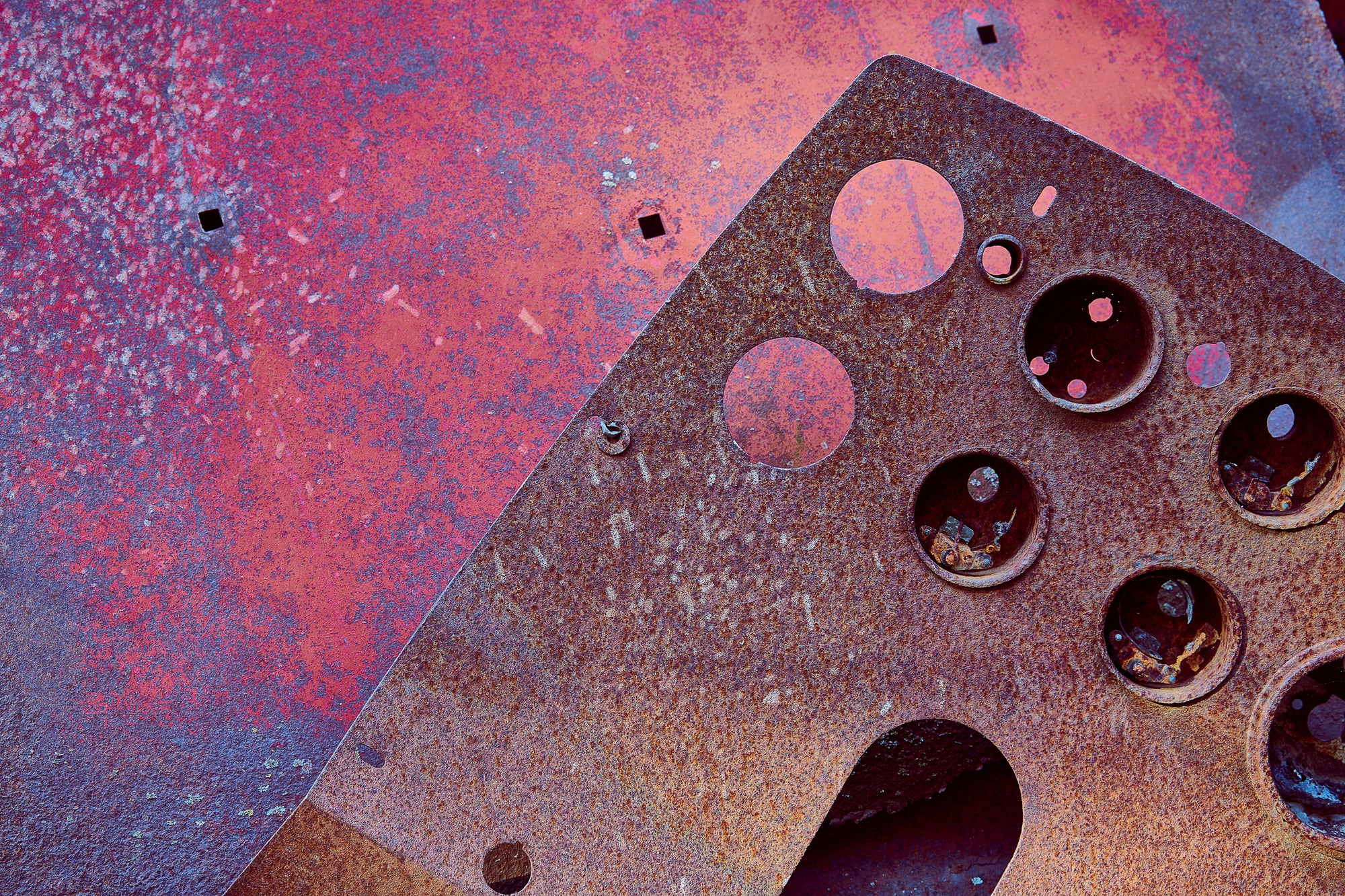 Detail on John Himmelfarb's full-size 2014 truck sculpture KB-3 is rusted metal, with multiple circular holes, in front of a pink and purple distressed metal background with three small square holes; photographer Rick Graves