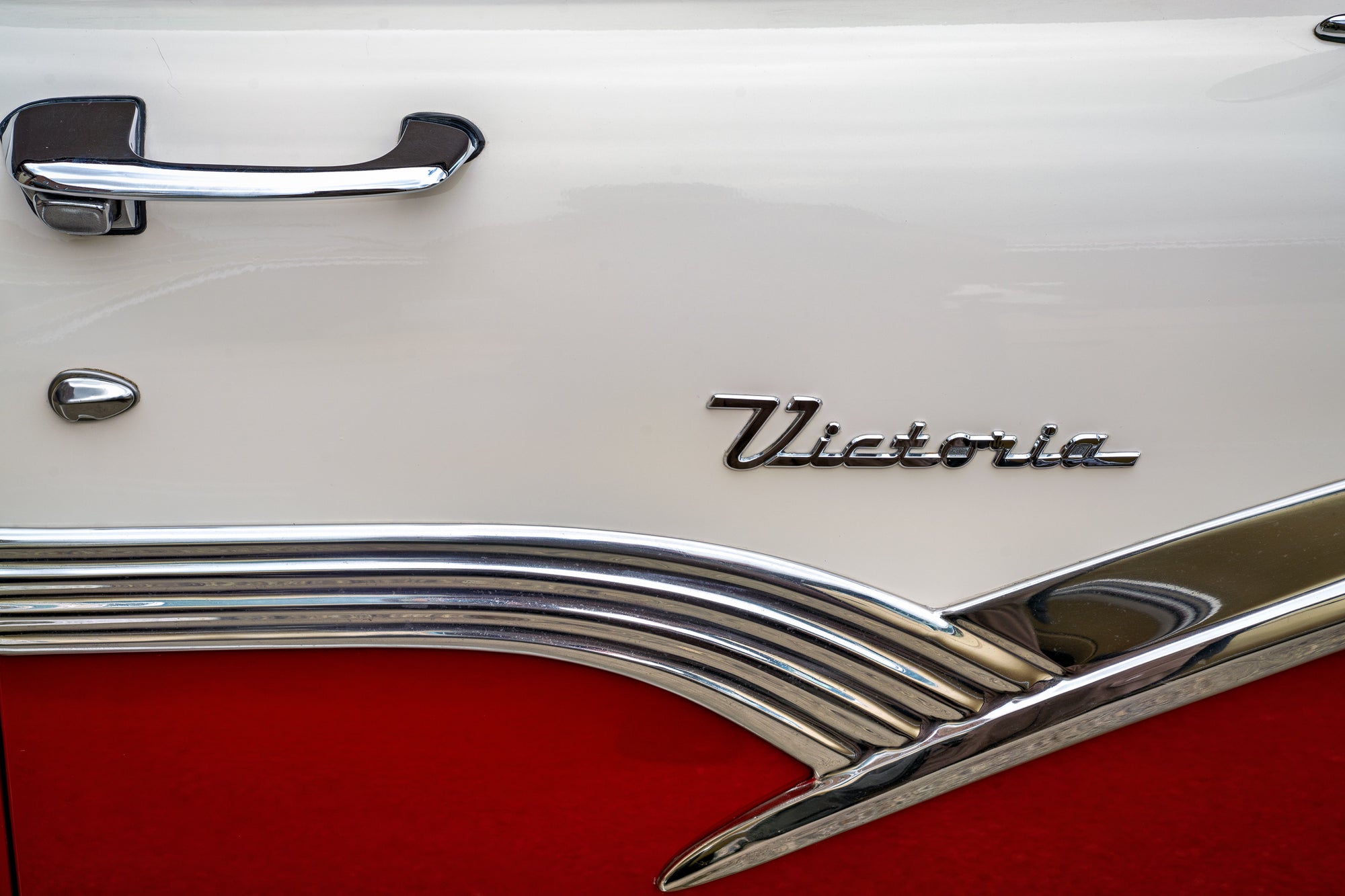 Close-up of a classic car door with 'Victoria' badge in chrome on a white and red background; photographer Rick Graves