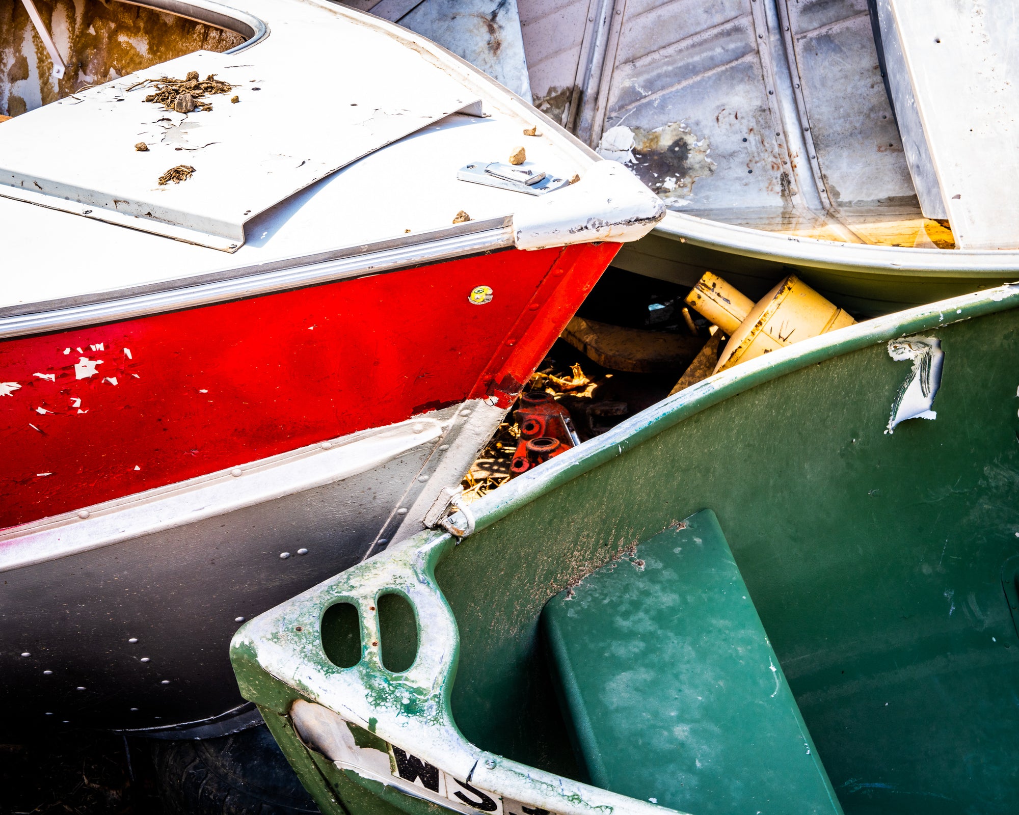 Close-up of three discarded boats with a red, green, and white one. Photographer Rick Graves