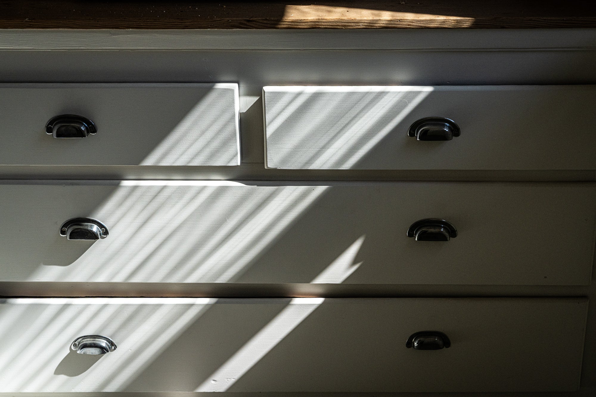 Close-up of a white dresser with silver handles dappled with sunlight and shadows; photographer Rick Graves