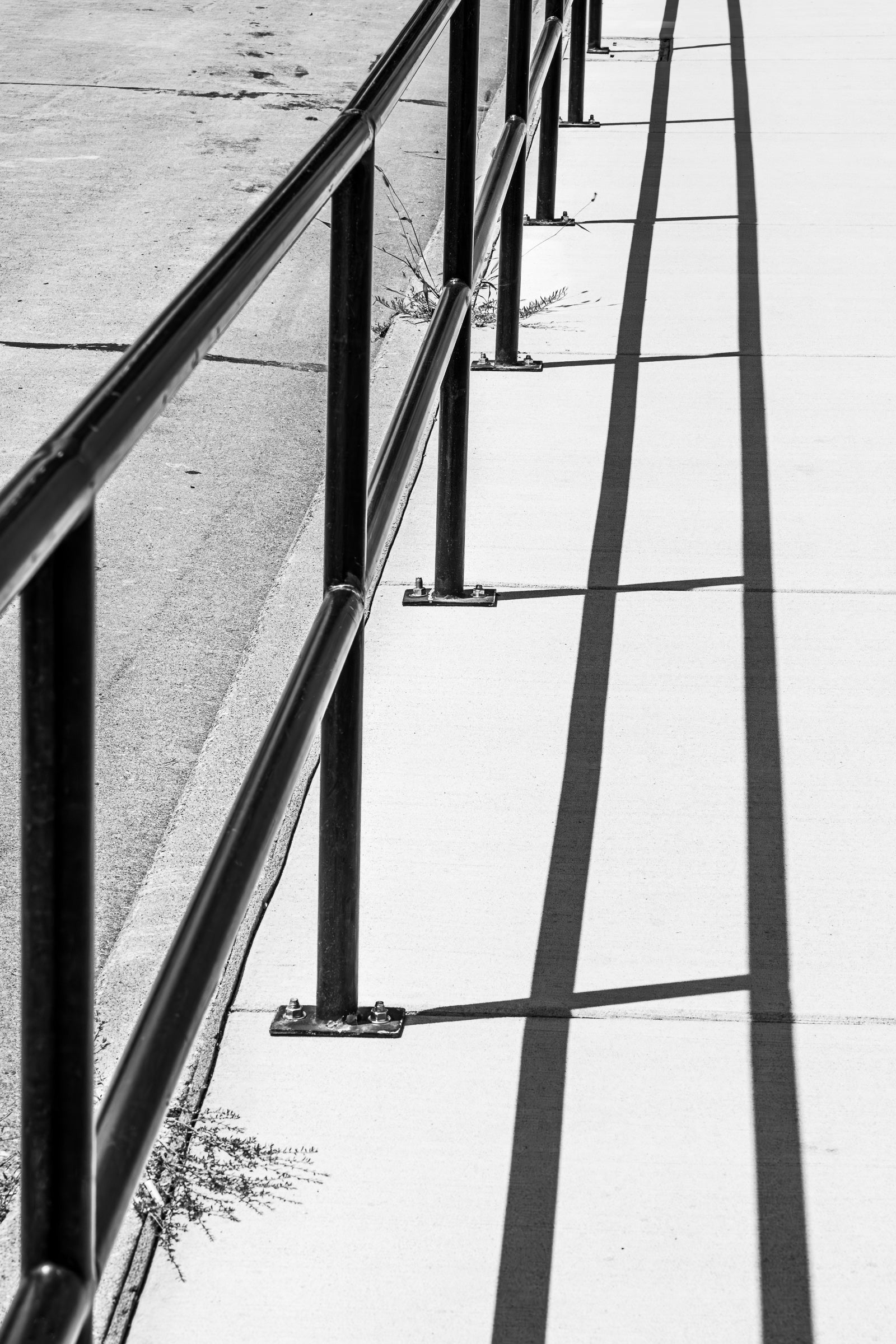 Black metal railing and perpendicular shadows on the sidewalk; photographer Rick Graves
