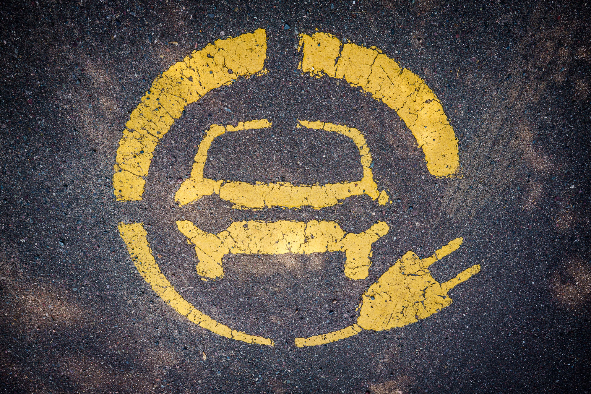 Weathered circular yellow electric vehicle charging symbol stenciled on asphalt; photographer Rick Graves