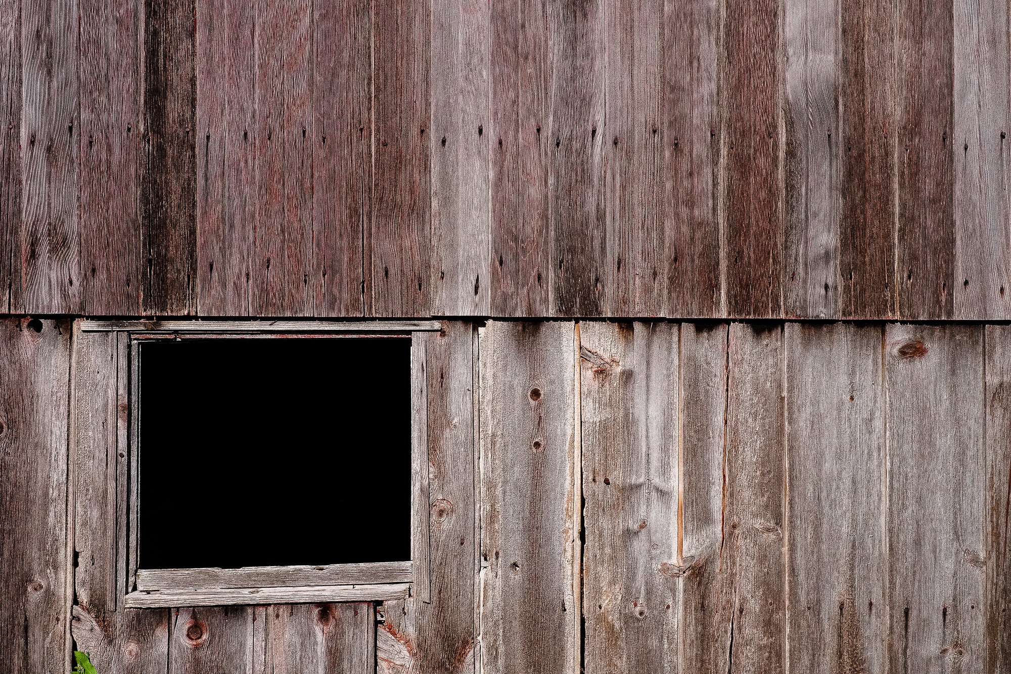 Weathered wood wall with a black void where a window once was; photographer Rick Graves