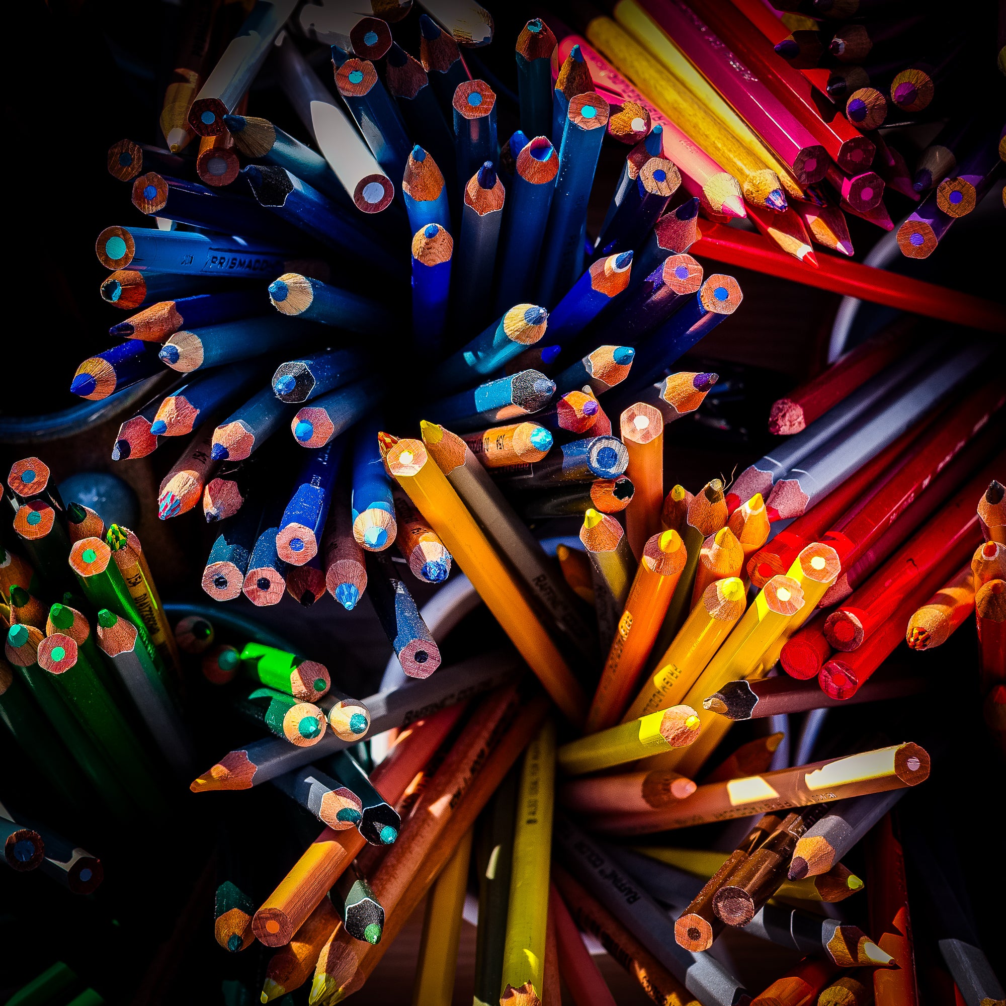 Colored pencils arranged in a circular pattern on a dark background; photographer Rick Graves