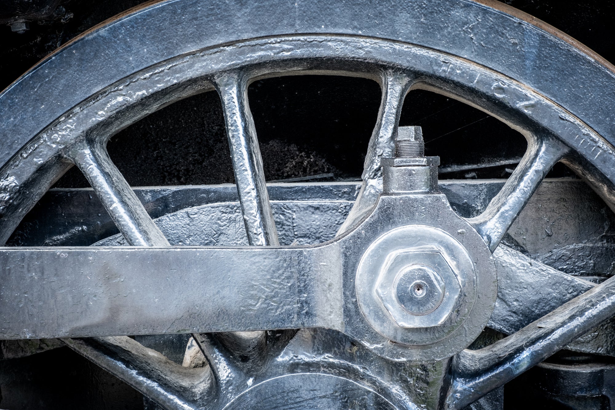Closeup of a vintage locomotive's wheelset, axle, and coupling rod painted with a silver preservative; photographer Rick Graves
