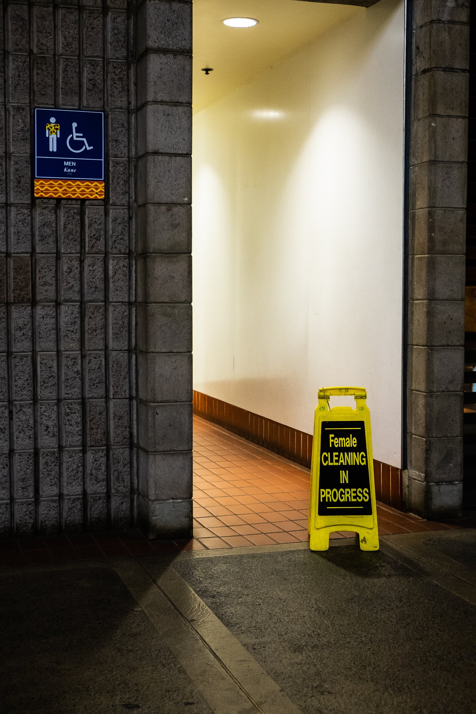 Entrance to a men's public restroom at the Maui Airport with a  'Female Cleaning in Progress' temporary sign on a tile floor. Photographer Rick Graves