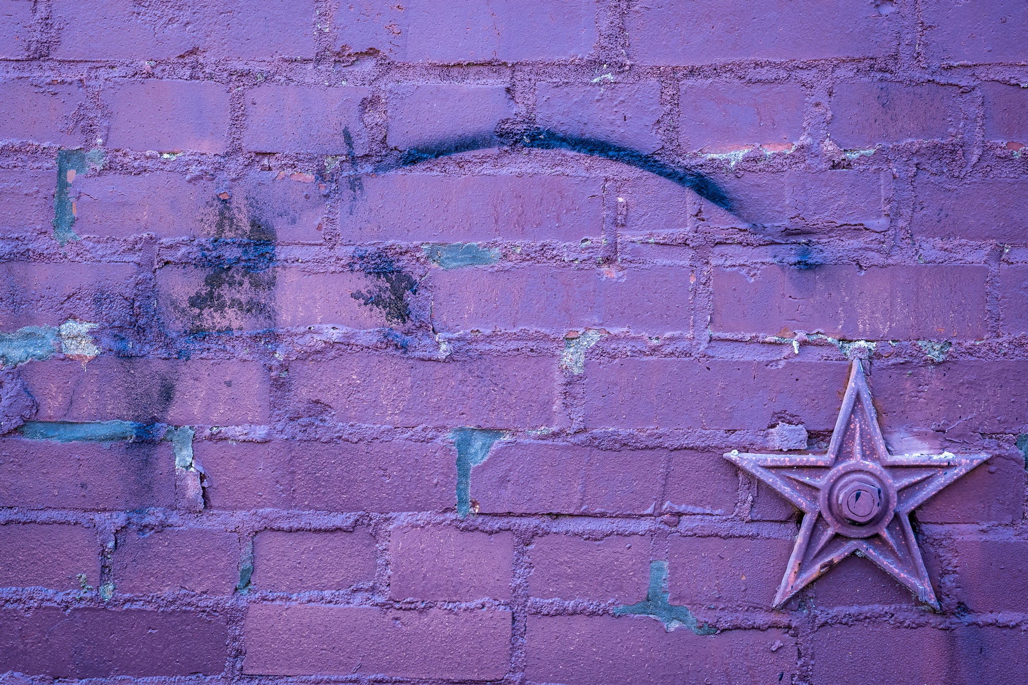 Blue curve, spray-painted on a purple brick wall, arcs to a metal star-anchor; photographer Rick Graves