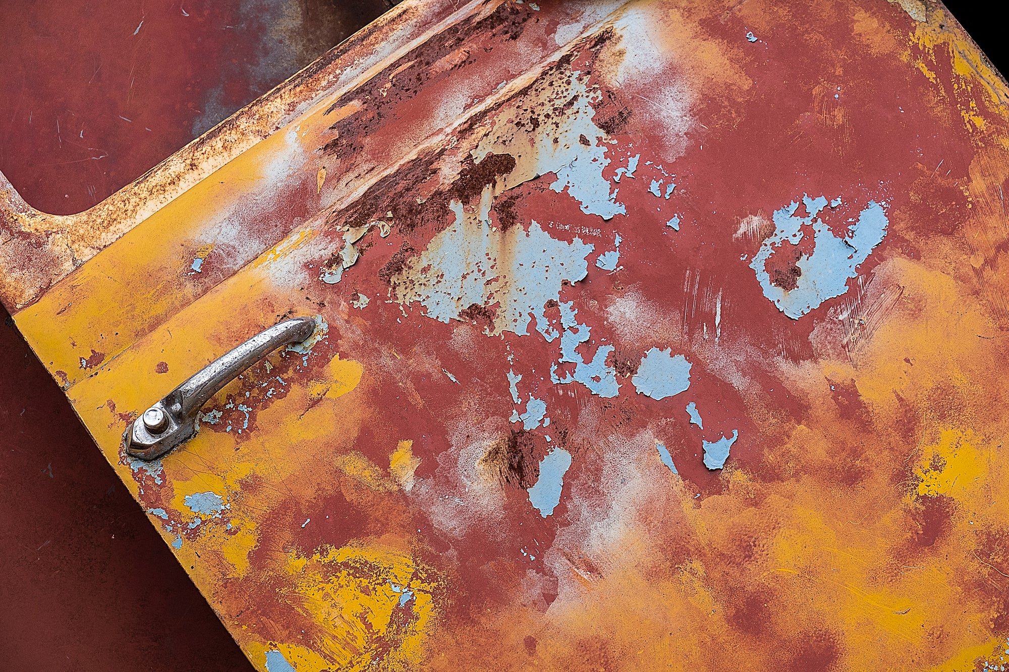 Rust and peeling red, blue, yellow, and orange paint on an old passenger-side truck door, mounted at an angle as part of a full-size 2015 truck sculpture by artist John Himmelfarb; photographed by Rick Graves with permission