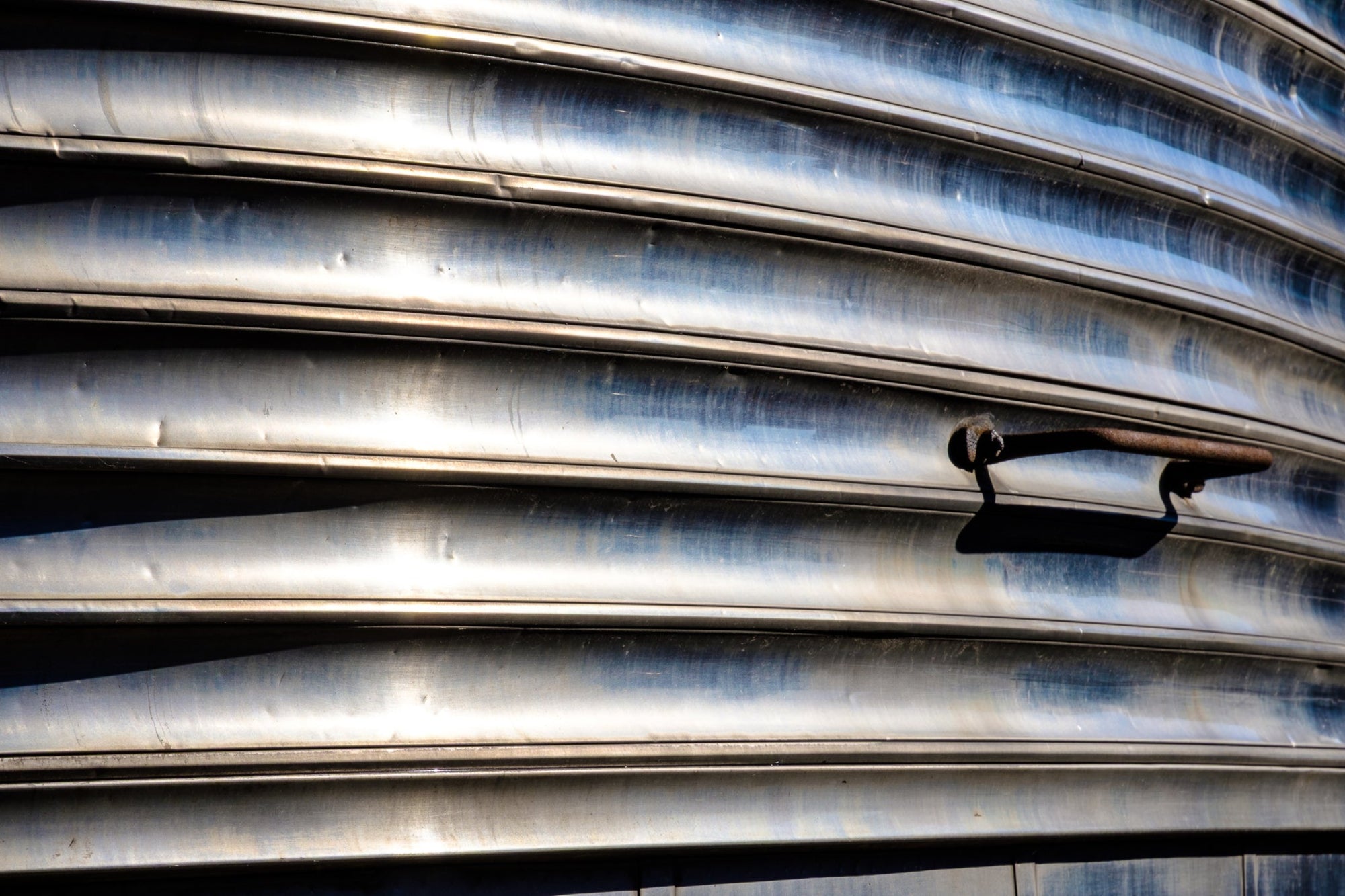 Rick Graves' tight detail of a vintage railroad passenger car showing silver ribbing and a rusty handle. 