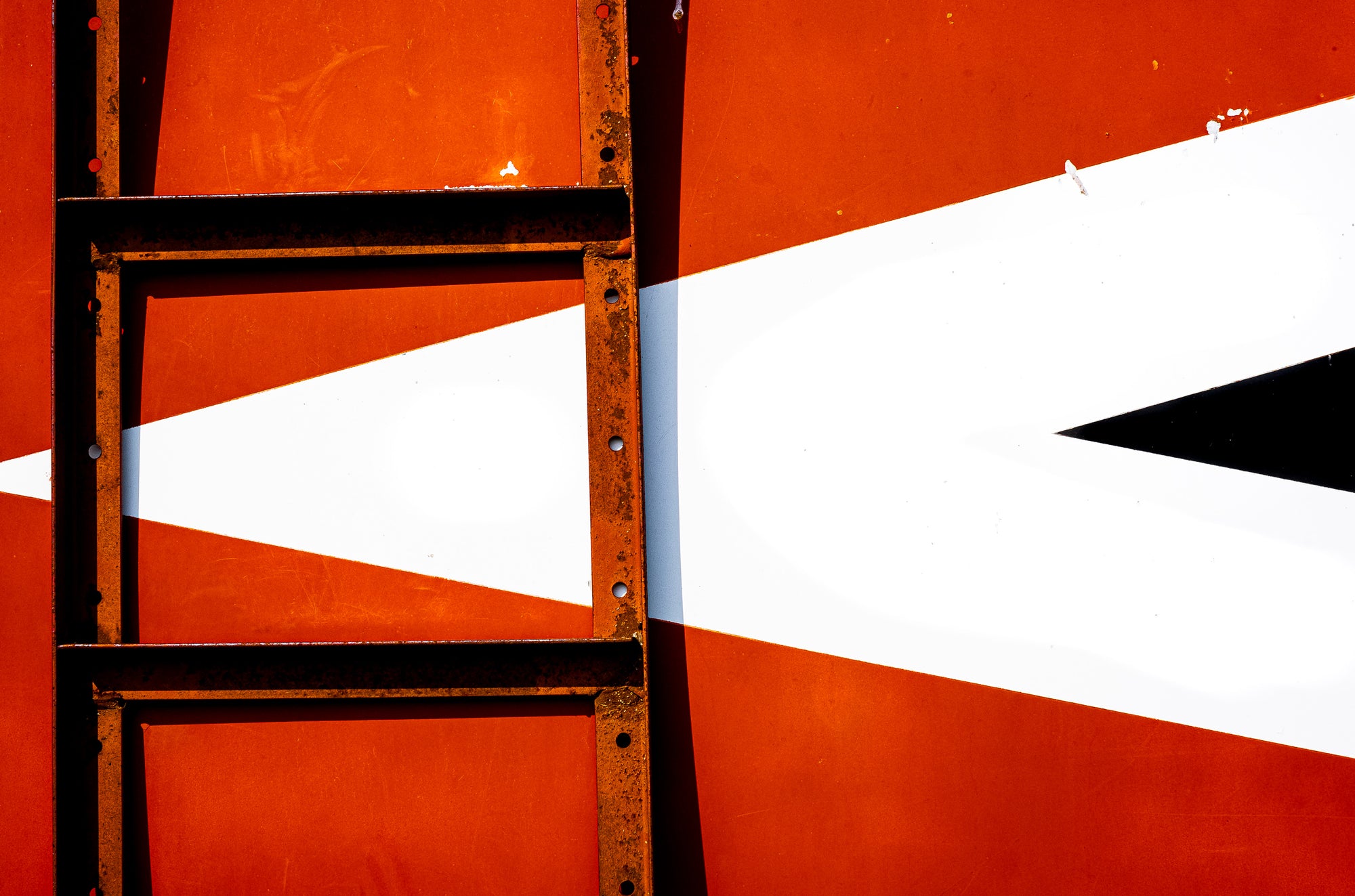 Close-up of Crysteel truck body with attached rusting ladder; box color is red with white and black nested triangular arrow pointing left; photographer Rick Graves