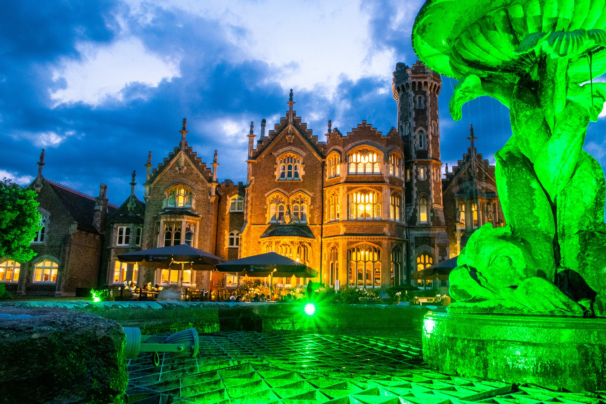 Grand home (used to film The Rocky Horror Picture Show) under a blue sky with a green fountain in the foreground; photographer Rick Graves