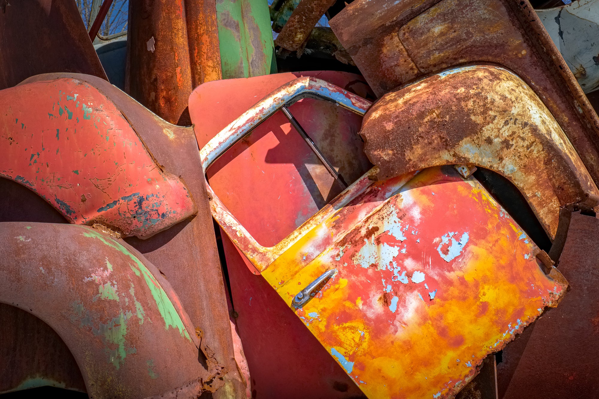 An assemblage of rusted vehicle components (fenders, hood, colorful passenger door) — part of John Himmelfarb's truck sculpture REMAINS. Photographed, with permission, by Rick Graves.