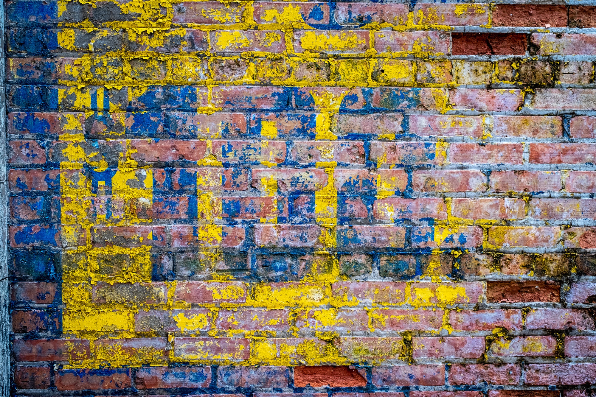 Distressed red brick wall with $100 painted in blue on yellow background; photographer Rick Graves