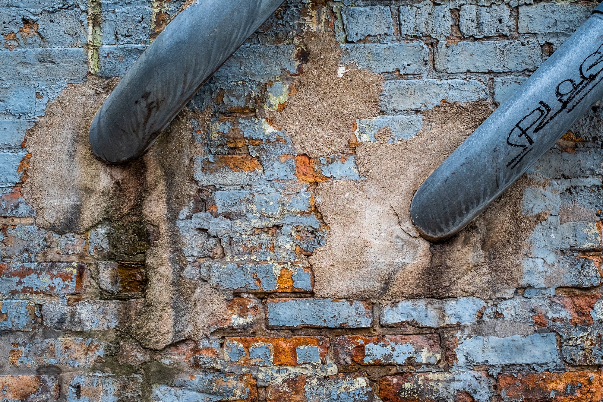 Two metal pipes protruding from an old brick wall with peeling paint; photographer Rick Graves