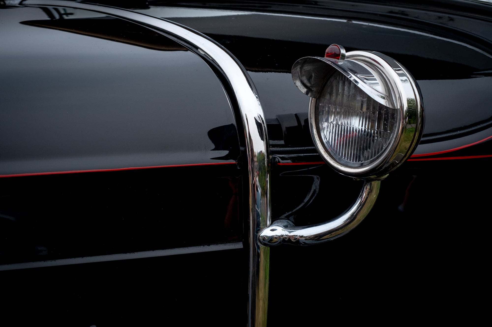 Close-up of a Ford Model T sidelight with chrome and red detailing on a black vehicle. The cap on the light makes it look like an eye. Photographer Rick Graves
