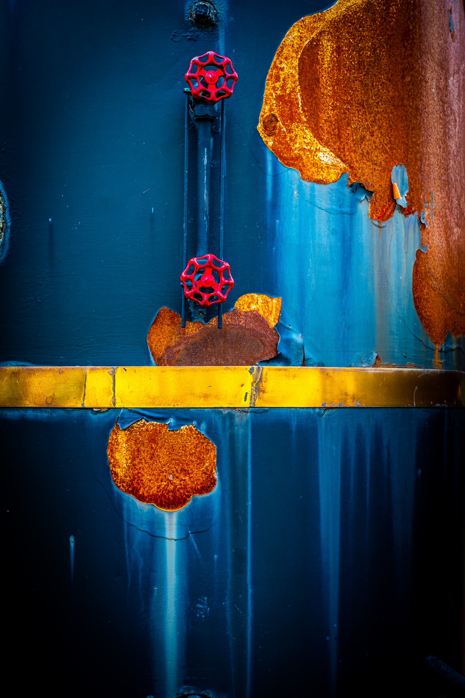 Rust and corrosion on the blue metal surface of a vintage Buffalo Springfield boiler with red valve handles; photographer Rick Graves