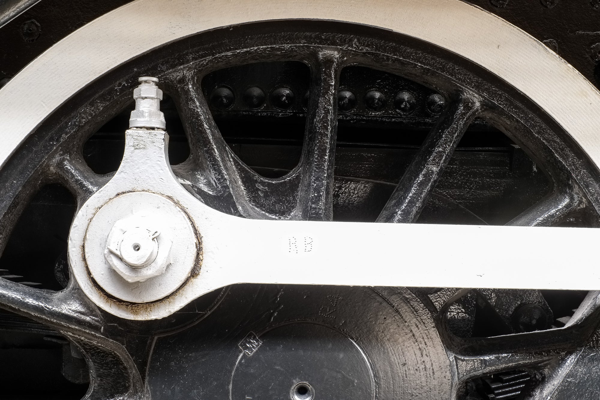 Closeup of a vintage locomotive's wheelset, axle, and coupling rod stamped with the letters RB; photographer Rick Graves