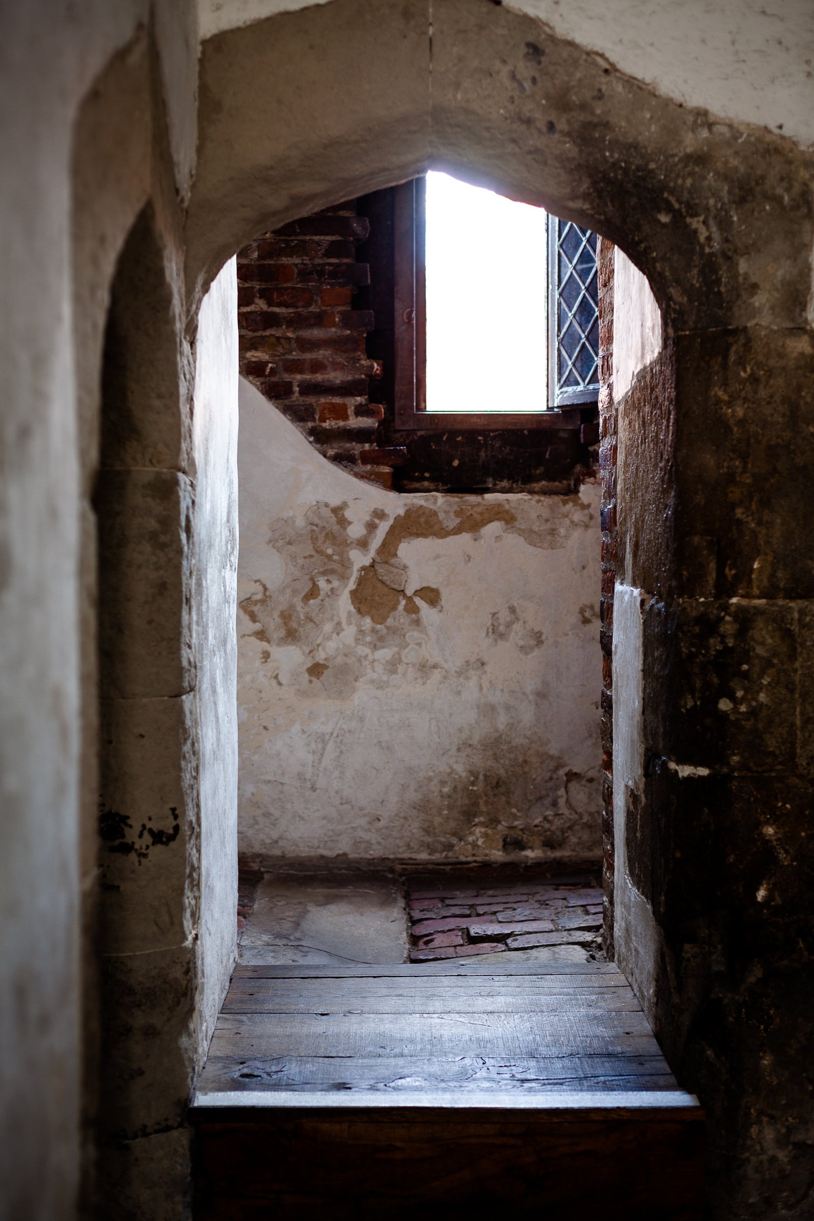 Passage through an archway into a dimly lit room with peeling paint and a window; photographer Rick Graves