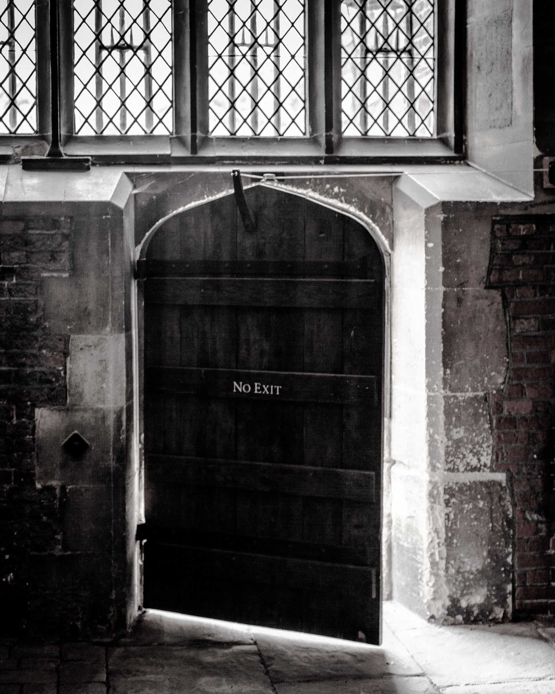 Dark wood arched door labeled 'No Exit' in a stone building with diamond-patterned glass above.