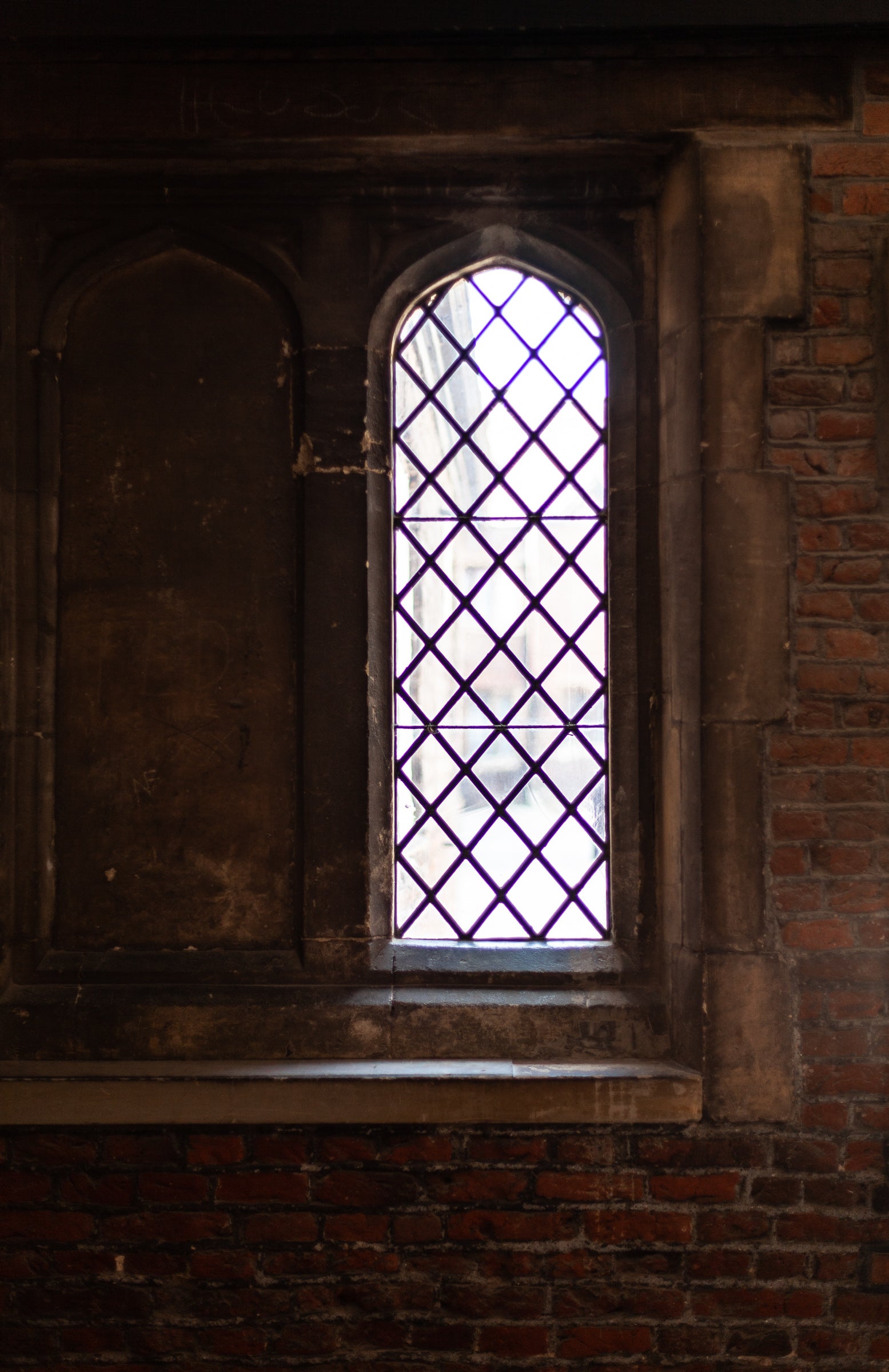 Narrow arched window with leaded glass in a brick wall; photographer Rick Graves