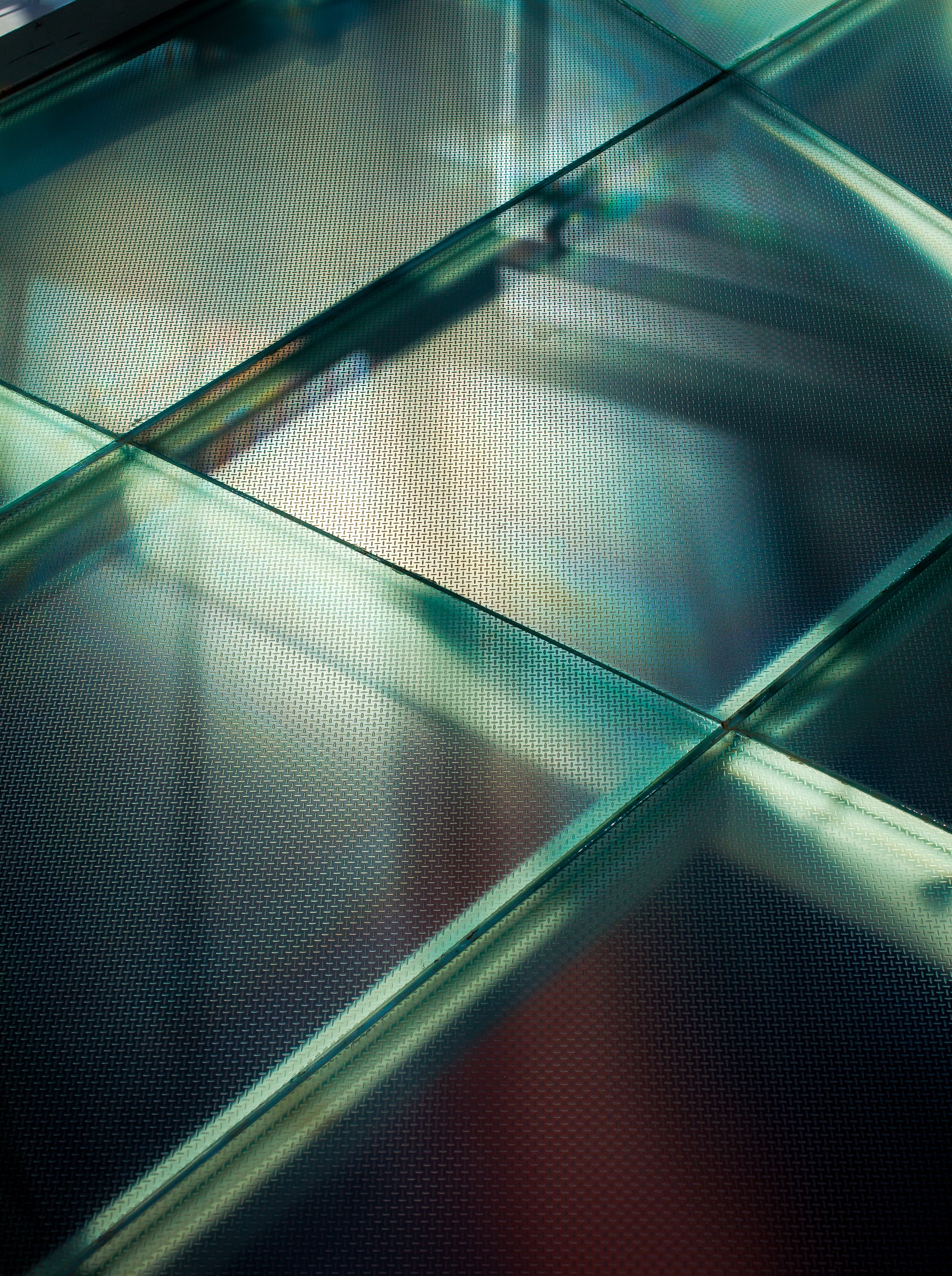 Close-up of a greenish glass floor with a metal grid support structure; photographer Rick Graves