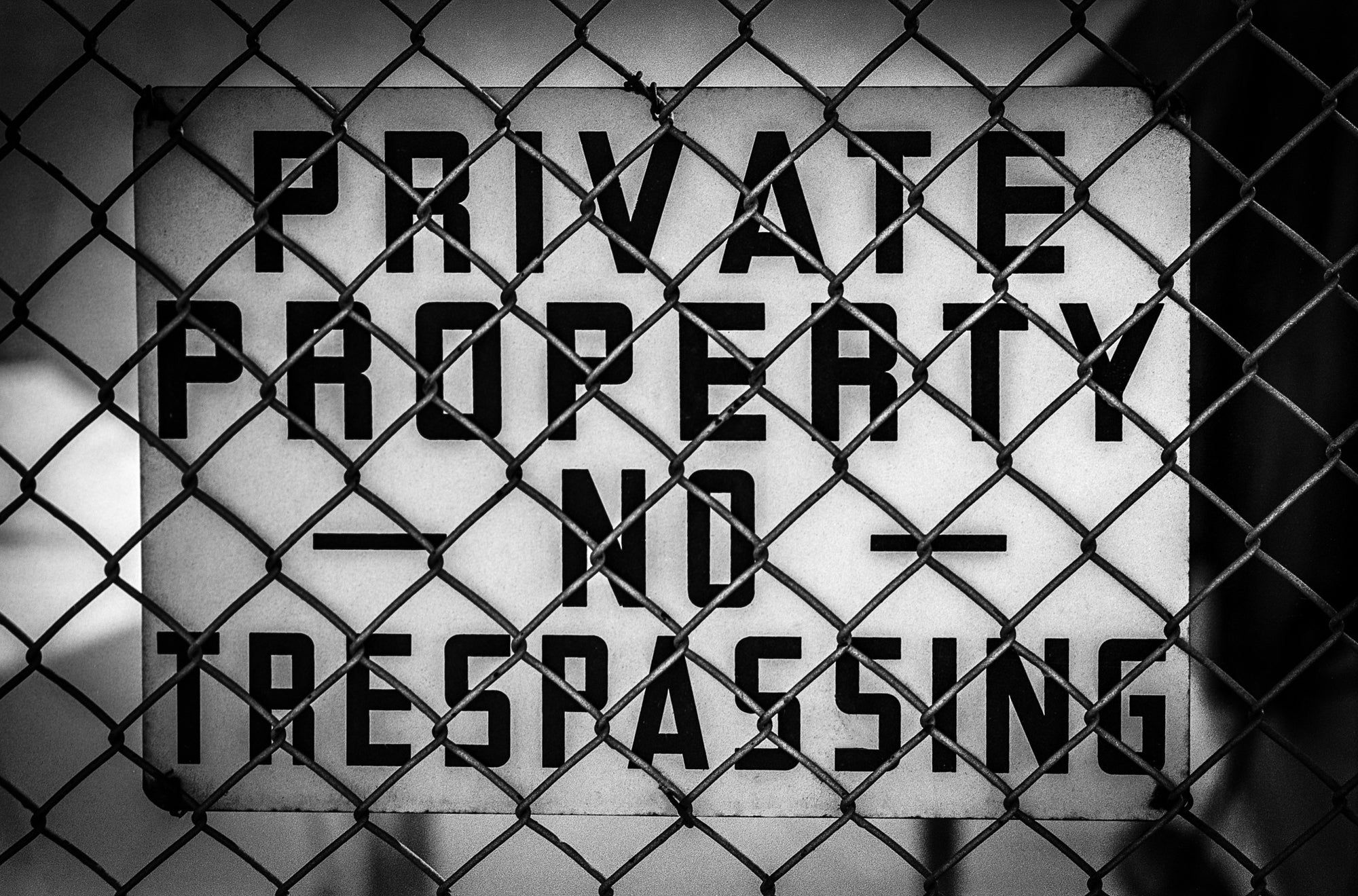 Black and white 'Private Property No Trespassing' sign behind a chain-link fence; photographer Rick Graves