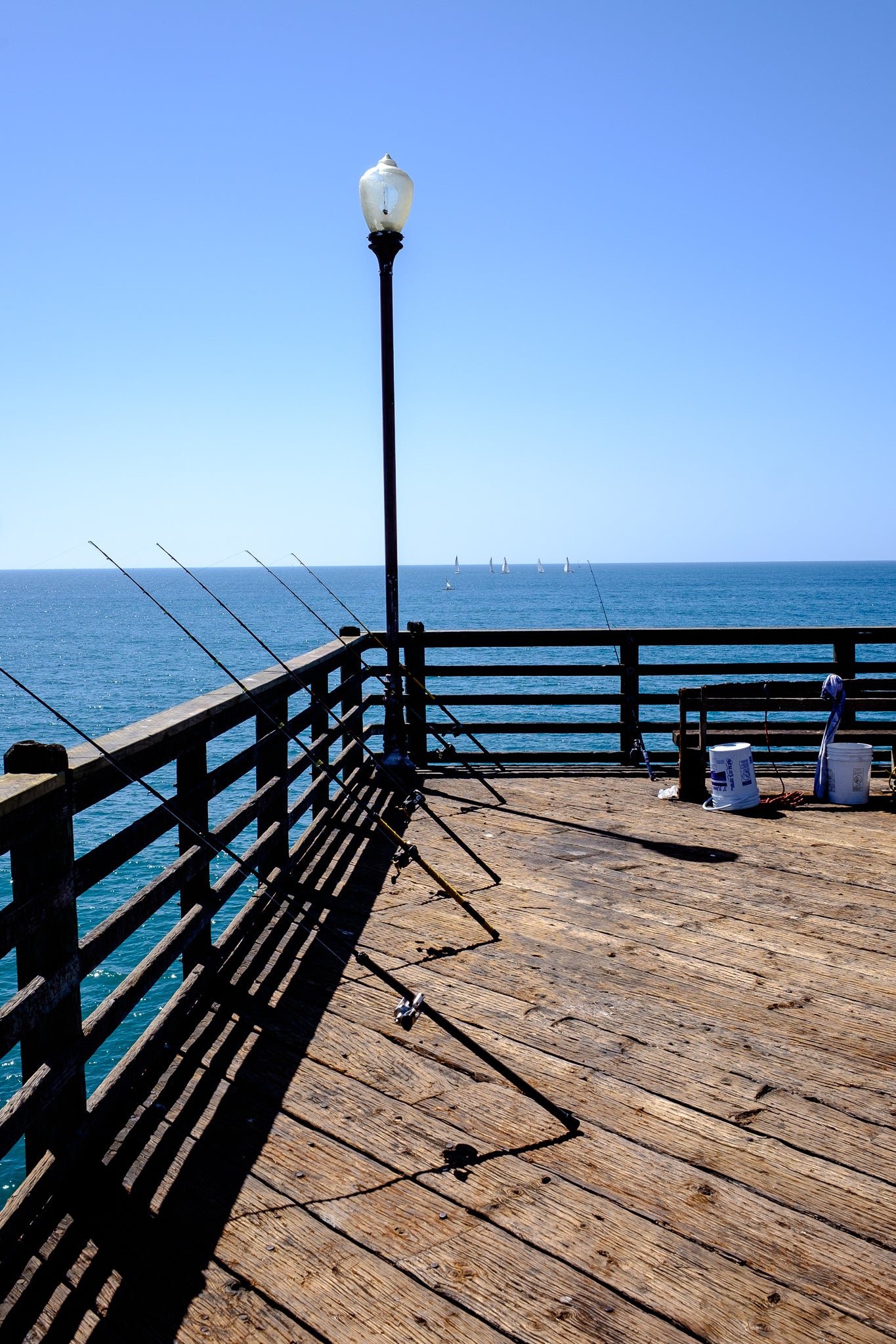 oceanside dock with fishing poles; sailboats on the horizon line; photo by Rick Graves