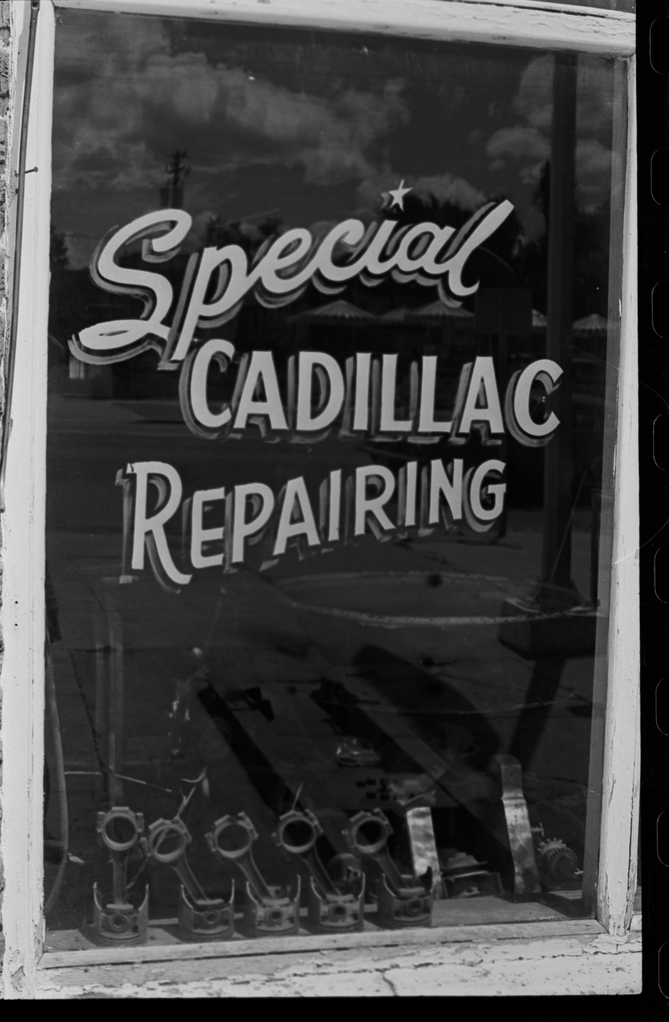 Black-and-white photo of a vintage sign for Special Cadillac Repairing in a glass window by Rick Graves.