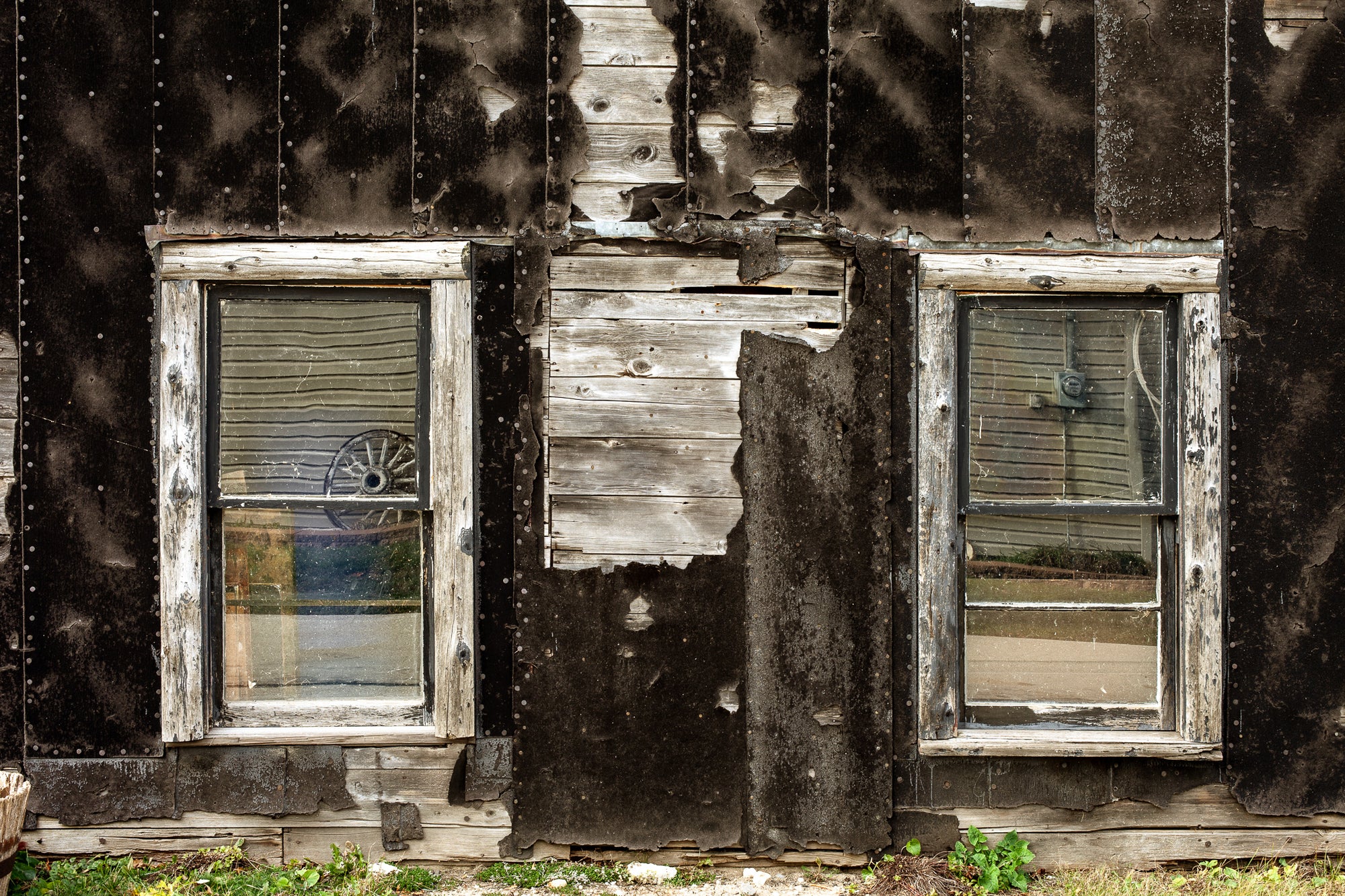 Battered wood building with peeling tarpaper and two windows. photo by ick Graves