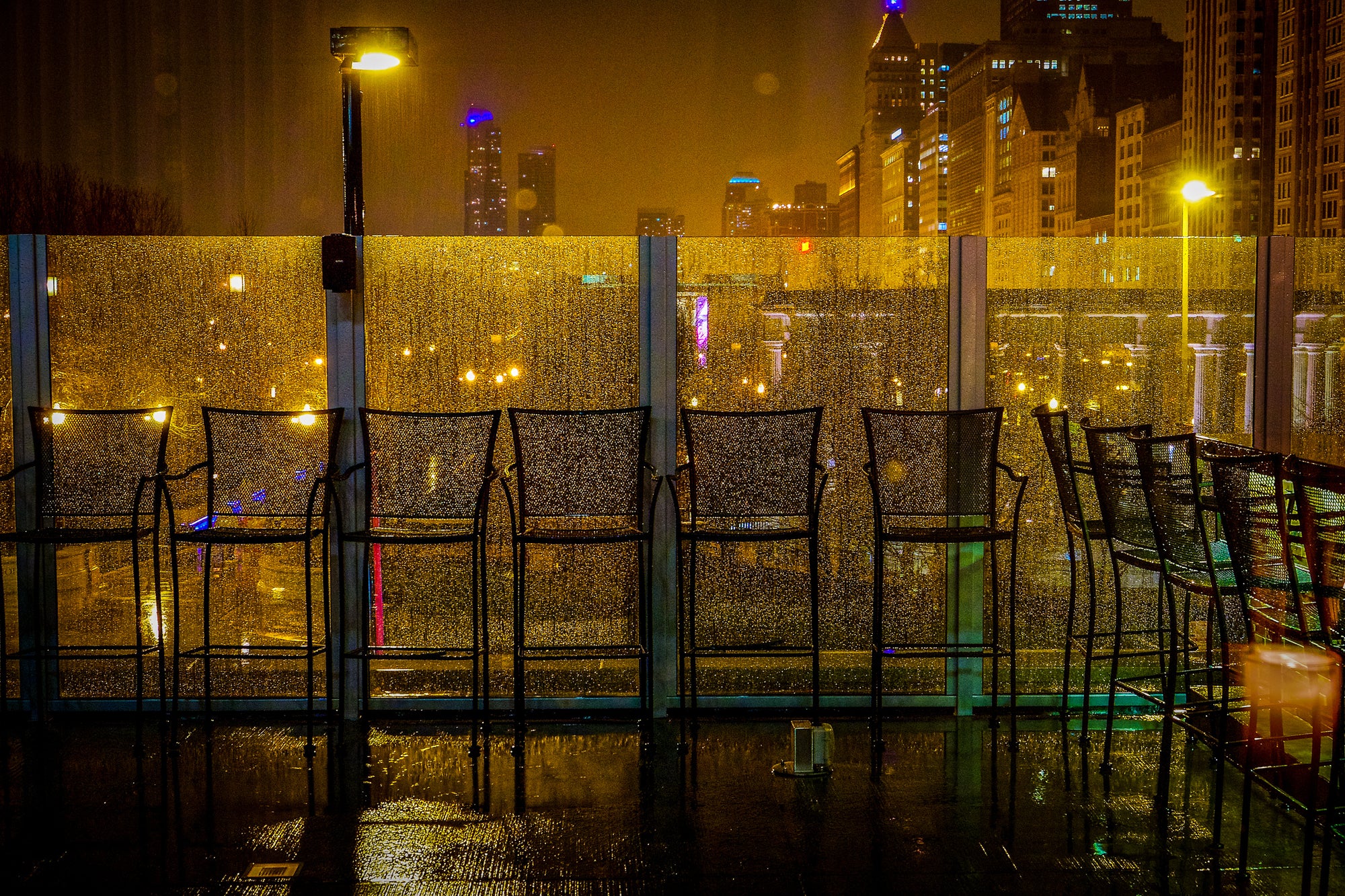 Empty seating in a row with the Chicago cityscape in the background at night in the rain.