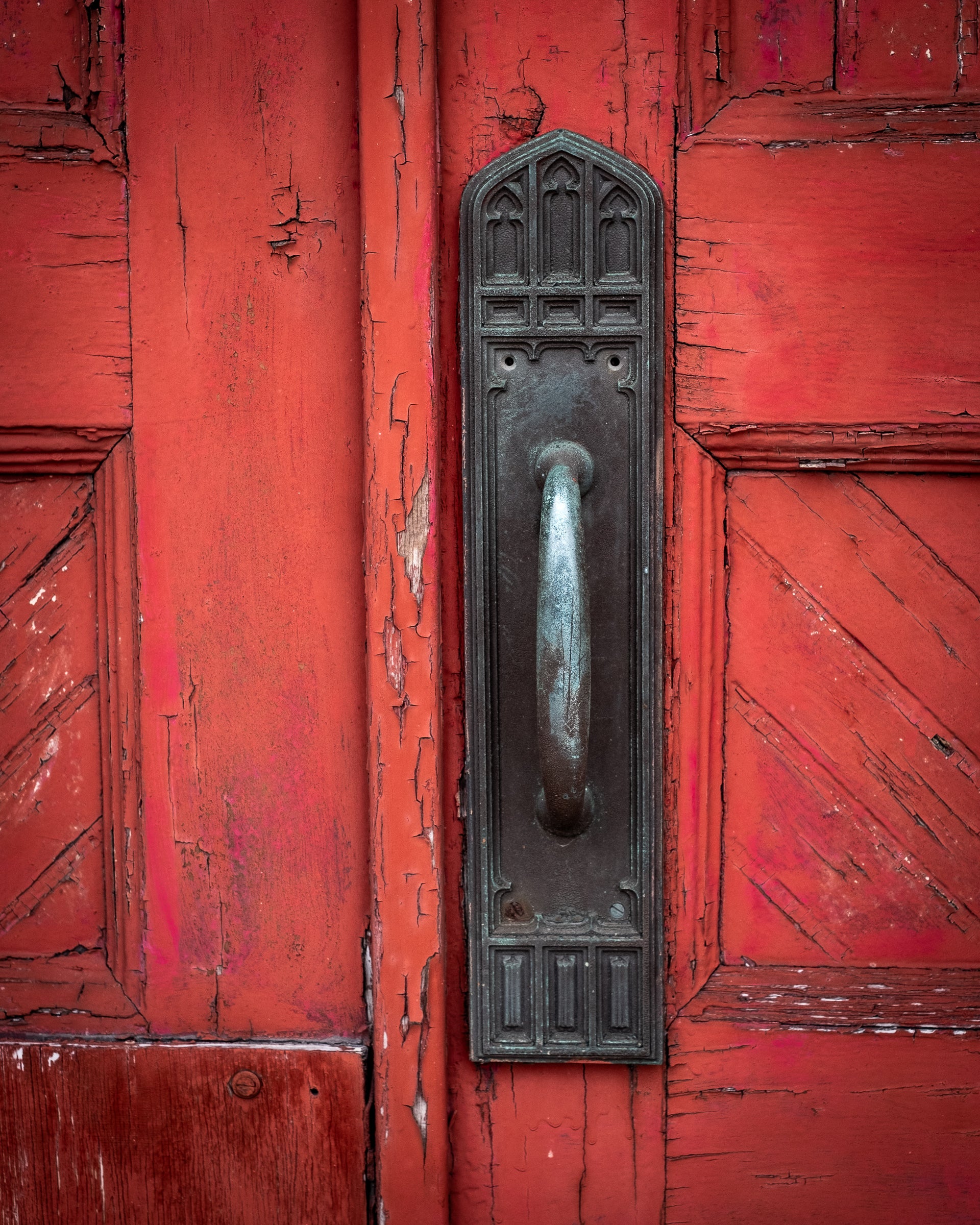 Close-up of a weathered red door with a metal handle and decorative plate; photo by Rick Graves.