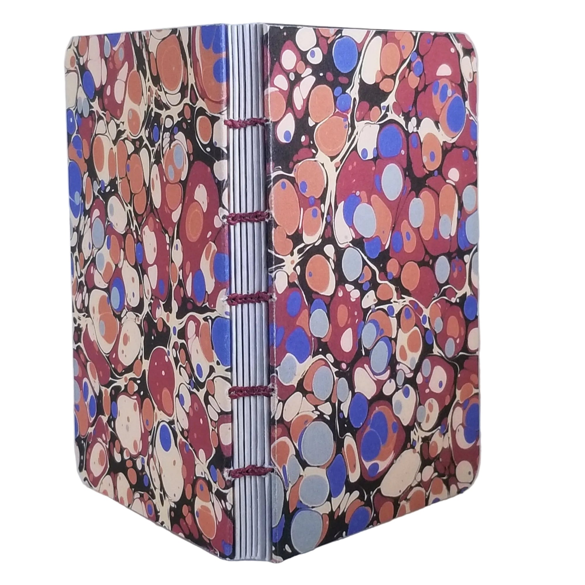 handmade small blank journal with predominantly blue and red printed marbling pattern, exposed spine, and bound with maroon waxed linen thread, ~4x5.5" 96 pages, shown on a white background