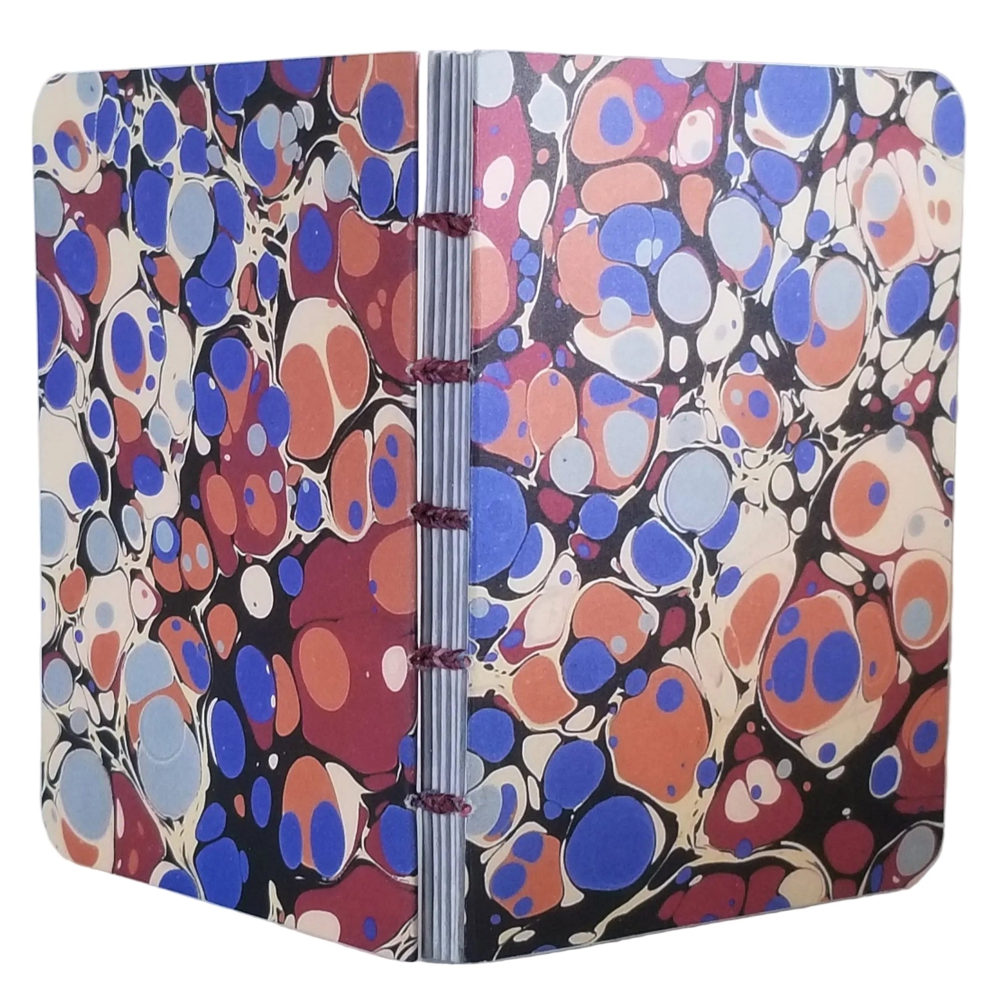 handmade coptic-bound blank notebook with multicolor printed marbled covers in blues, maroon, cream, and orange, bound with dark red waxed linen thread, ~4x5.5" 96 pages, shown on a white background