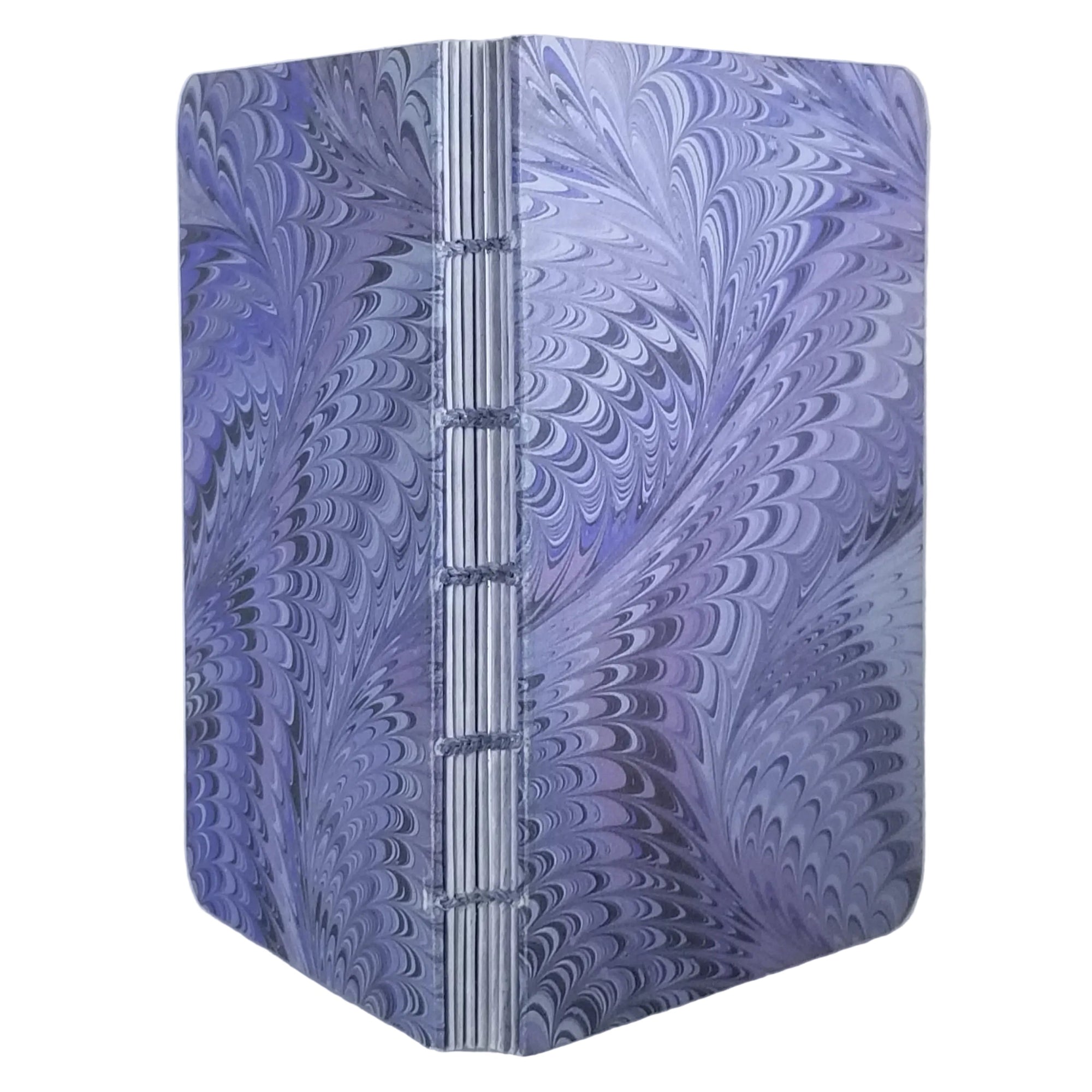 handmade small blank journal with predominantly lavender and purple printed paper marbling pattern, and matching waxed linen thread, ~4x5.5" 96 pages, shown on a white background